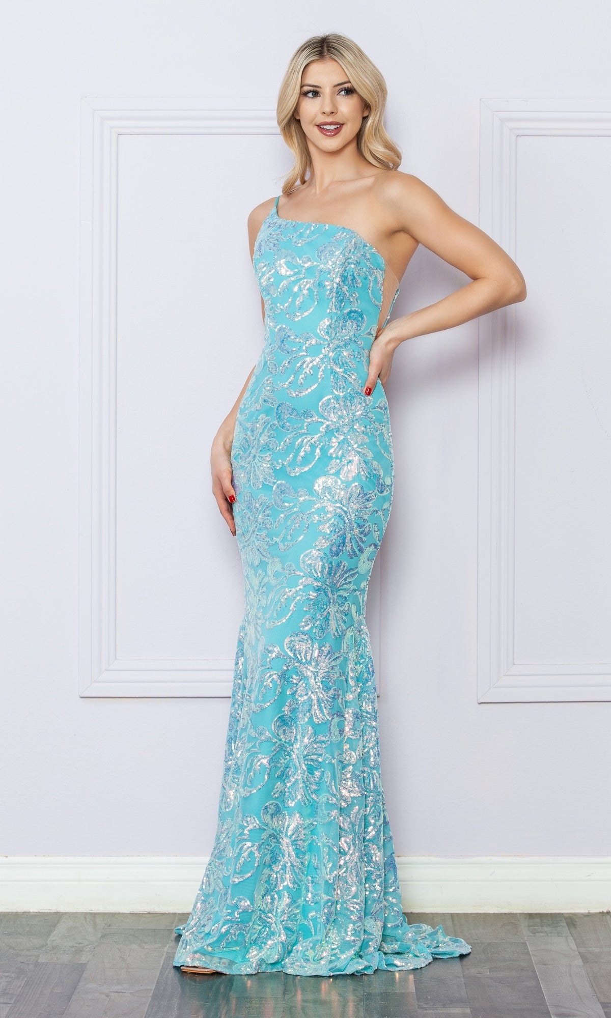 A woman poses against a light-colored wall in the One-Shoulder Long Sequin-Print Prom Dress R1308, featuring a light blue, floor-length design with silver floral patterns and sequin-print details.